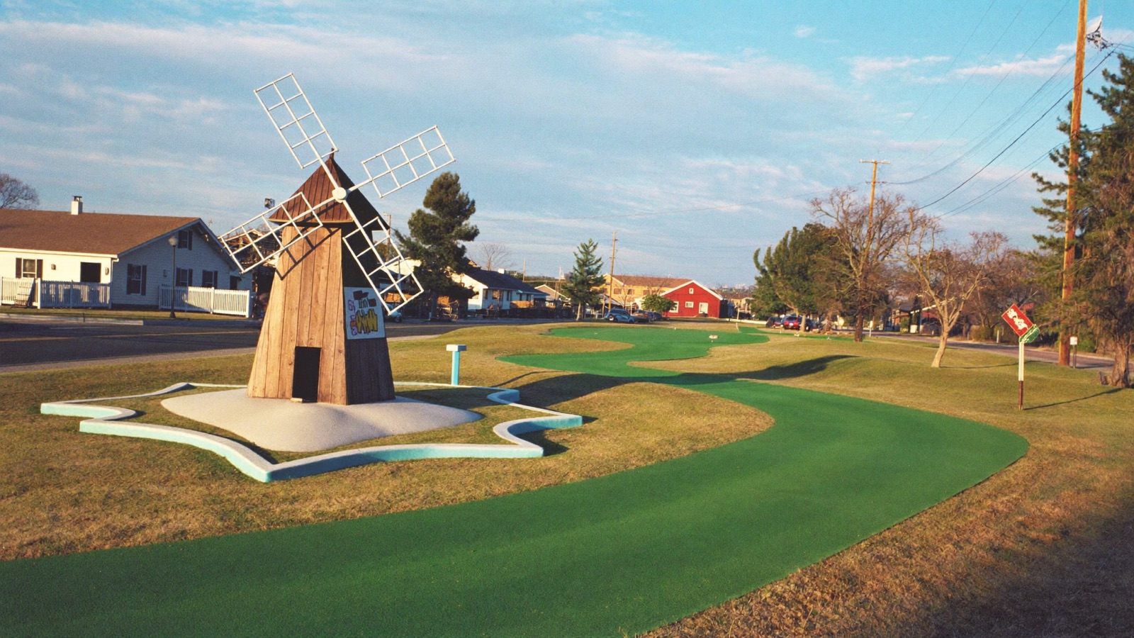 The Wormburner Mini Golf course at golden hour, with the big red windmill turning over the turf.